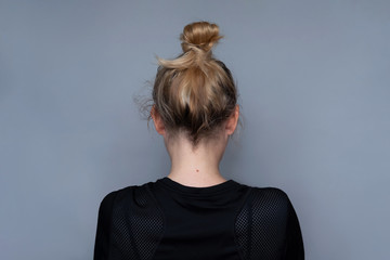 Young girl simple hairstyle back view. Fashionable and simple hairdresser work. Fashion model, trendy woman. Blonde long hair in top bun close-up photo. Elegant and everyday look for girls