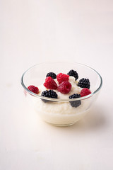 Semolina pudding porridge dessert with  blackberry and raspberry berries in glass bowl, breakfast, white wooden background, isolated