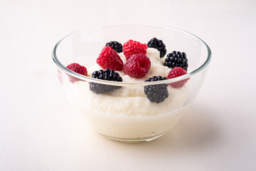 Semolina pudding porridge dessert with  blackberry and raspberry berries in glass bowl, breakfast, white wooden background, isolated