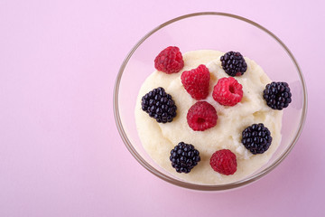 Semolina pudding porridge dessert with  blackberry and raspberry berries in glass bowl, breakfast, pink background, isolated