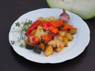 Beautiful vegetable stew with courgettes, tomatoes, peppers, carrots and grilled cheese baked are in a white plate on a wooden table close-up. Appetizing and healthy vegetable food.