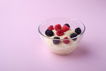 Semolina pudding porridge dessert with  blackberry and raspberry berries in glass bowl, breakfast, pink background, isolated