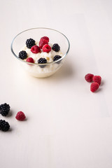 Semolina pudding porridge dessert with  blackberry and raspberry in glass bowl near with scattered heap berries on white wooden background, breakfast, isolated