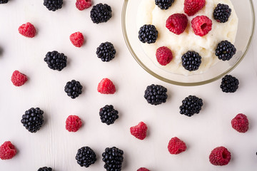 Semolina pudding porridge dessert with  blackberry and raspberry in glass bowl near with scattered heap in order berries on white wooden background, breakfast, isolated, top view
