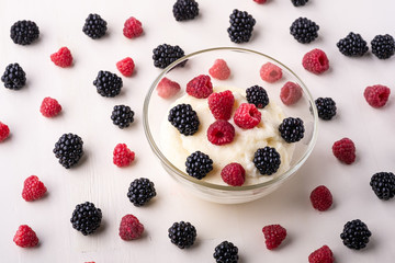 Semolina pudding porridge dessert with  blackberry and raspberry in glass bowl near with scattered heap in order berries on white wooden background, breakfast, isolated, selective focus