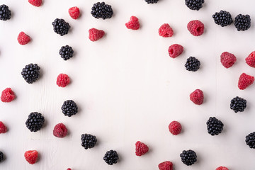 Blackberry and raspberry scattered heap in order berries on white wooden background copy space, isolated, texture