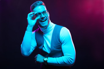 Young handsome model posing in a studio in a trendy neon light. Fashionable man in a stylish suit. Vibrant color. Bright colorful light effects. Disco style. Overlay. Gel filter. Supersaturated