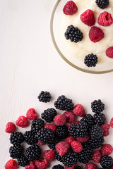 Semolina pudding porridge dessert with  blackberry and raspberry in glass bowl near with scattered heap berries on white wooden background, breakfast, isolated, top view