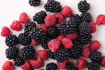 Blackberry and raspberry scattered heap berries on white wooden background copy space, isolated, texture top view
