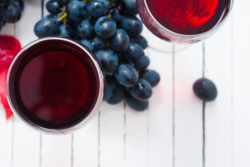 two glasses of red wine and grapes on white wooden table background
