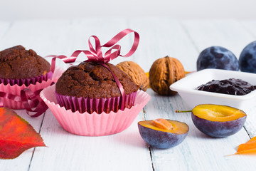 chocolate muffins and jelly, plums, walnuts on white wooden table