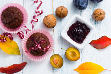 chocolate muffins and jelly, plums, walnuts on white wooden table