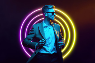 Young handsome model posing in a studio in a trendy neon light. Fashionable man in a stylish suit....