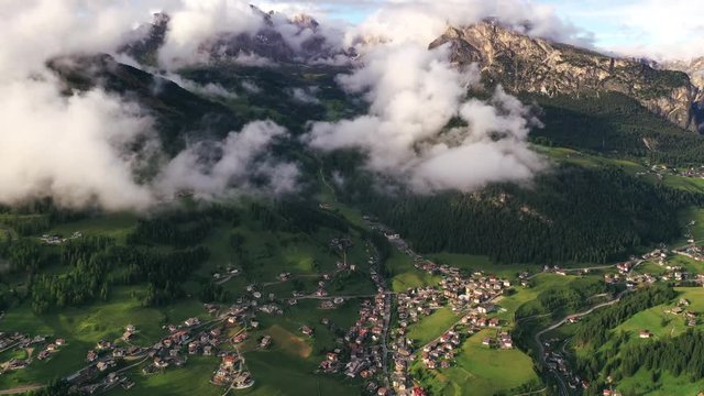 Hyperlapse aerial view of small town near the mountains during sunset. Clouds covering mountains and moving fast
