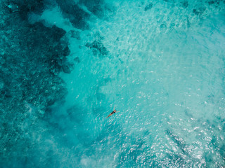 Aerial view woman in lack  bikini lying on transparent turquoise water surface on beach