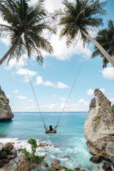 Young girl swinging on a swing overlooking the blue sea. Travel adventure on paradise tropical island. A young girl swinging on a swing between palm trees on the beach of a tropical island