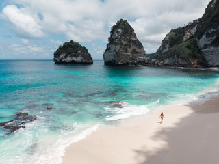 Fototapeta premium Woman walking alone on amazing tropical white sand beach. Aerial drone view from above. Tropical background and travel concept. Flying high above unrecognizable tourist girl