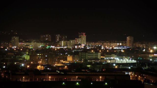 Night city skyline timelapse. Top aerial panoramic view of modern city from tower rooftop. Road junction traffic. Lights flicker in windows. Residential flats,factory pipes with smoke