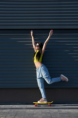 Portrait of positive young attractive girl wearing yellow top and blue jeans with yellow skateboard.