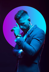 Young handsome model posing in a studio in a trendy neon light. Fashionable man in a stylish suit. Vibrant color. Bright colorful light effects. Disco style. Overlay. Gel filter. Supersaturated