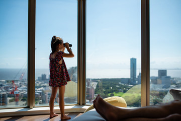 マンションの窓から双眼鏡で外を眺める女の子