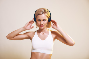 Naklejka premium Love this music. Cute and sporty woman adjusting headphones and looking at camera while standing against pink background.