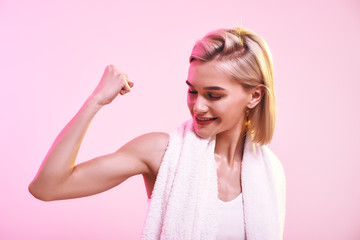 You are stronger than you think! Attractive young sporty woman showing her bicep and smiling while standing against pink background
