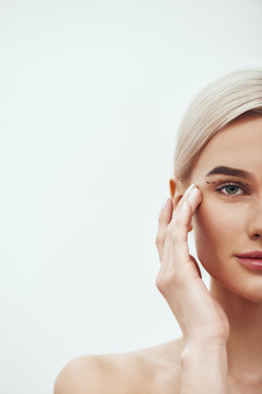 Plastic Surgery Operation. Cropped photo of pretty and young blonde woman touching her face with black surgical lines on eyelids and looking at camera