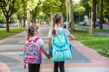 Back to school education concept with girl kids, elementary students, carrying backpacks going to class