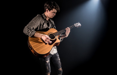 Obraz premium Guitarist, music. A young man plays an acoustic guitar on a black isolated background