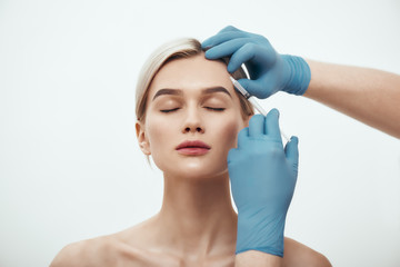Cosmetic injection. Portrait of young pretty woman keeping eyes closed while doctors hand in blue medical gloves making an injection of botox in her face