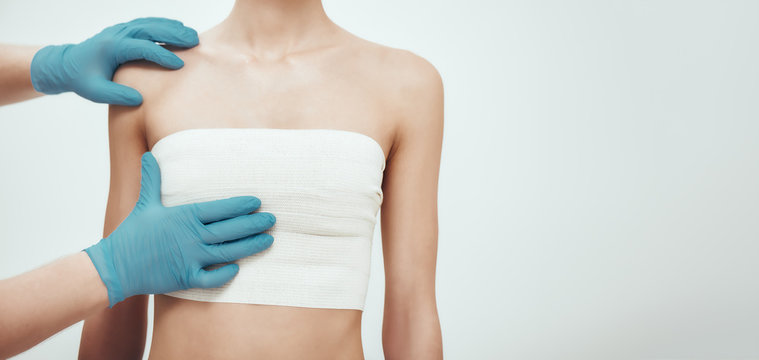 Increase your breast size. Cropped photo of woman waiting for plastic surgery while surgeons in blue medical gloves measuring her breast