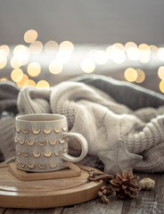 Coffee cup over Christmas lights bokeh in home on wooden table with sweater on a background and decorations. Holiday decoration, magic Christmas