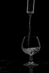 Water is poured into a transparent glass from a bottle on a dark background