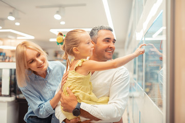 Naklejka premium Girl touching window while looking at parrots with parents