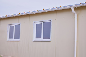 White plastic rain guttering system. Guttering drainage pipe exterior. Background of sandwich panel 