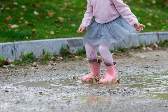 Little girl in rubber boots and tutu dress jumping in puddle. Water is splashing from kid feet as she is jumping and playing in the rain.
