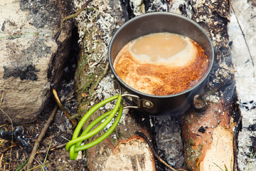 Coffee near the fire outdoors. Adventure, travel, tourism and camping concept. Coffee from mug at camp. Coffee cooked over a campfire on the nature.