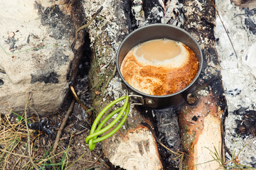 Coffee near the fire outdoors. Adventure, travel, tourism and camping concept. Coffee from mug at camp. Coffee cooked over a campfire on the nature.