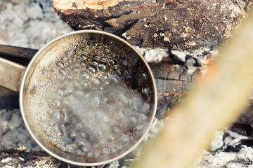 Coffee near the fire outdoors. Adventure, travel, tourism and camping concept. Coffee from mug at camp. Coffee cooked over a campfire on the nature.