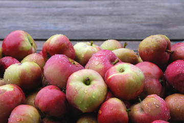 Food background of small red apples pile wet from rain against wooden backdrop. Selective focus, natural seasonal fruits, autumn harvest