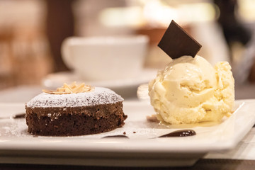 Chocolate lava cake with vanilla ice cream in a white plate on blurred restaurant background.
