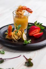 Crispy Shrimp in Kataifi Crust and Thyme with Champagne Sauce in glasses and strawberries lie on a black plate on a white woody background