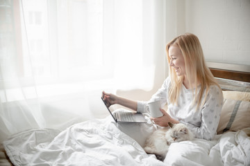 Work from home concept . Blonde Giirl typing and using laptop. Hygge with fluffy cat, pajama and coffee cup. Horizontal copyspace