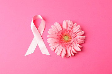 Pink awareness ribbon and gerbera on color background, space for text.