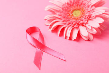 Pink awareness ribbon and gerbera on color background, space for text.
