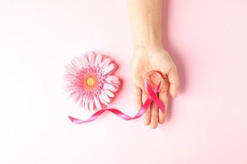 Female hand with pink awareness ribbon and gerbera color background