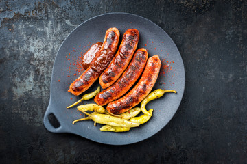 Traditional barbecue German Bratwurst with hot sauce and peperoni as closeup on a modern design cast iron plate