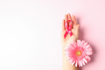 Female hand with pink awareness ribbon and gerbera color background