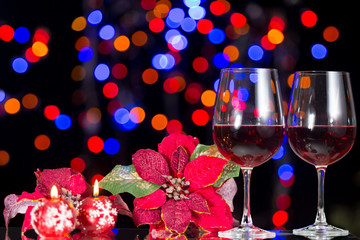Still life decoration of elements making a Christmas motive for the Holidays containing Christmas candles, Christmas flower, glasses of wine and Christmas lights bokeh for celebration.
